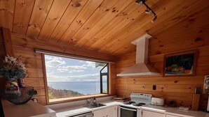 A kitchen with wooden ceiling, white cabinets, a stove, and a view of the sea. - Lake views, boating, skiing and hot pools (Omori)