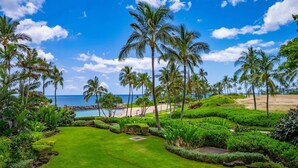 A well-maintained garden with palm trees, a neatly trimmed lawn, and a view of the beach. - Nalu Collection 2/2 Oceanfront Living~Luxurious Amenities (Kapolei)
