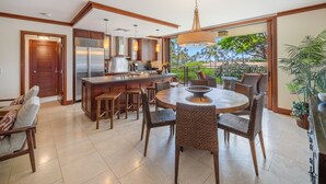 A modern kitchen with a central island, bar stools, and a dining table with chairs. - Nalu Collection 2/2 Oceanfront Living~Luxurious Amenities (Kapolei)