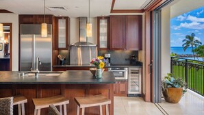 A modern kitchen with a large island, stainless steel appliances, wooden cabinets, and a view of the ocean. - Nalu Collection 2/2 Oceanfront Living~Luxurious Amenities (Kapolei)