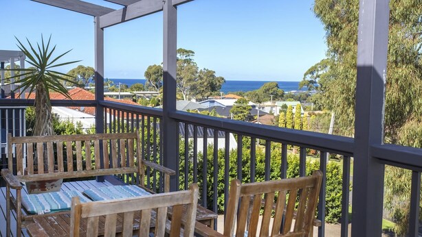 A wooden deck with a table and chairs, overlooking a residential area and the ocean. - Horizons in Mollymook (Mollymook Beach)