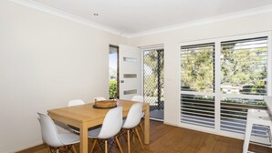 A dining area with a wooden table, white chairs, and a basket. - Horizons in Mollymook (Mollymook Beach)