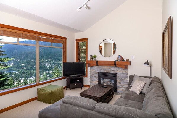 A living room with a fireplace, a television, and a large window offering a mountain view. - BLUFFS 6 | 3 Bed 2 Bath Townhouse | Ski-In/Out | Breathtaking Views | Hot Tub (Whistler)