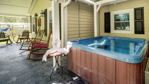 Een hottub met houten buitenkant, een schommelstoel en een tafel met glazen en handdoeken.
