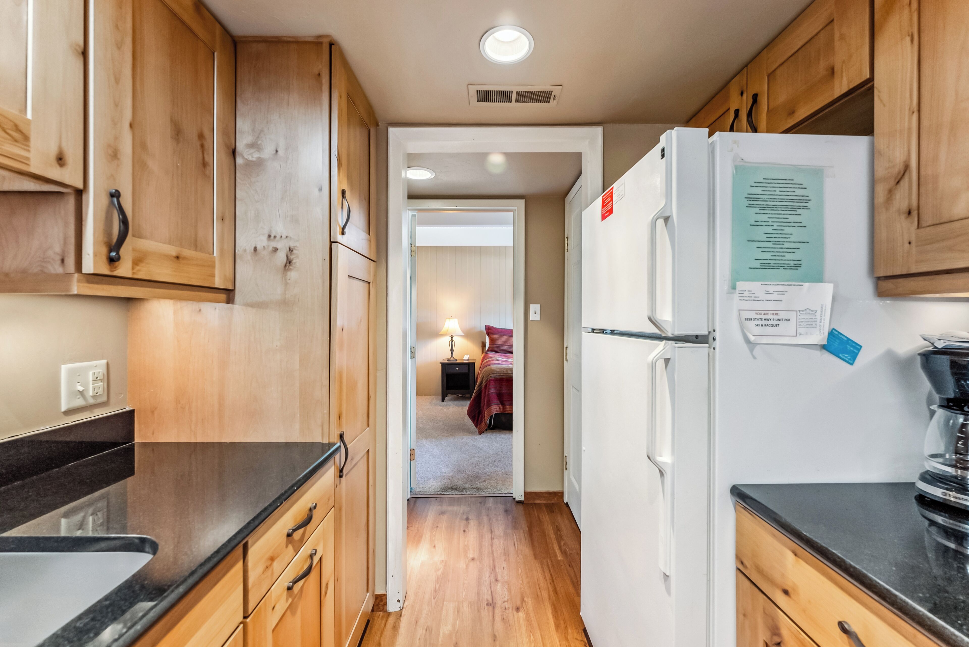 A narrow kitchen with wooden cabinets, a white refrigerator, and a black countertop.