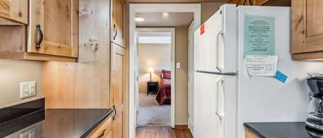 A narrow kitchen with wooden cabinets, a white refrigerator, and a black countertop.
