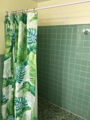 A bathroom with a shower curtain featuring a tropical leaf pattern, green tiled walls, and a tiled floor. - KCB-access Private Cabana Club, Dock on Canal, PET Friendly, Pickle ball courts (key colony Beach)