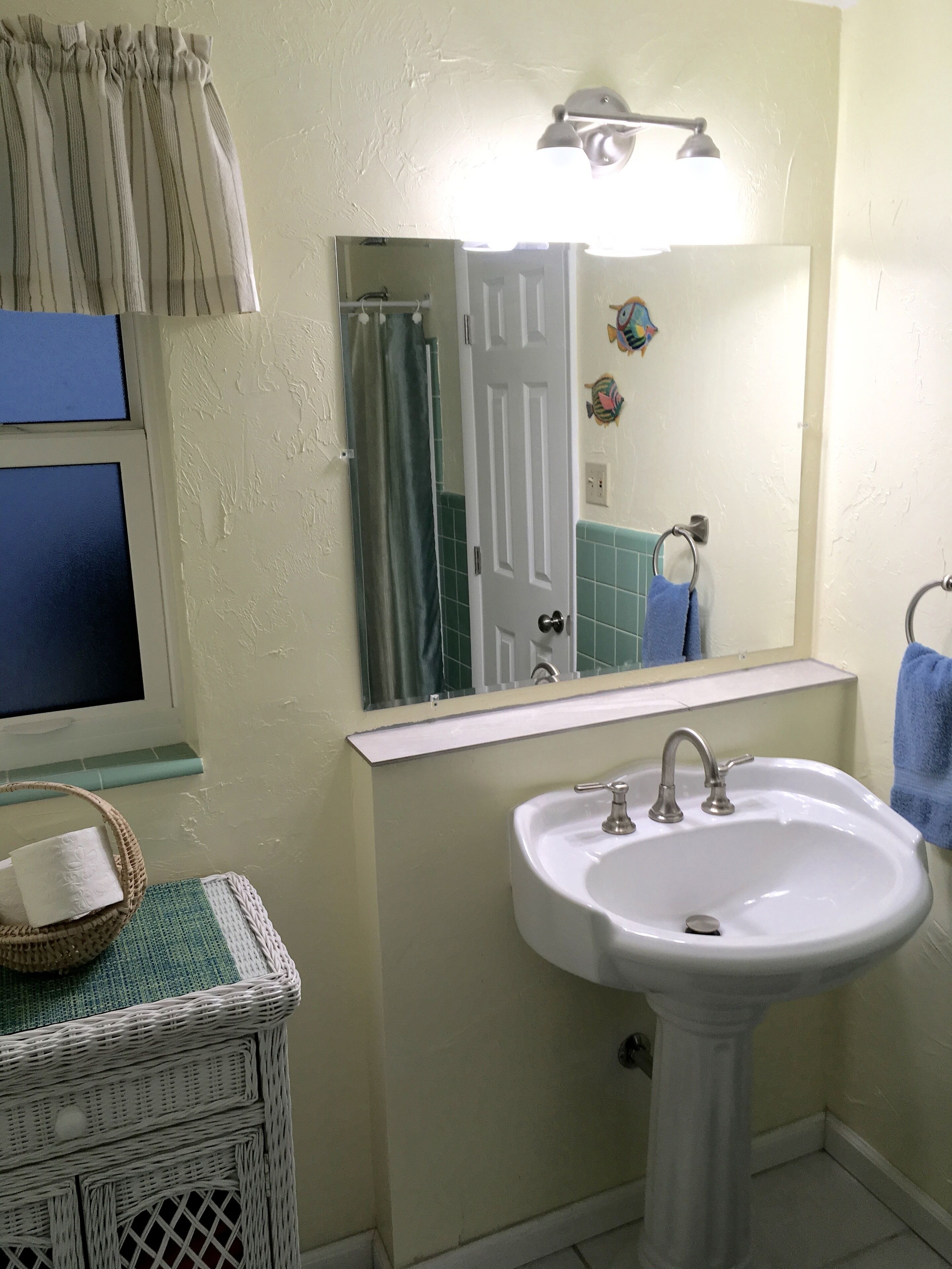 A bathroom with a white sink, a mirror, a shower curtain, and a window with blinds.