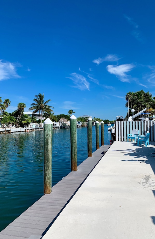 A waterfront dock with a concrete walkway, palm trees, and boats in the background. - KCB-access Private Cabana Club, Dock on Canal, PET Friendly, Pickle ball courts (key colony Beach)