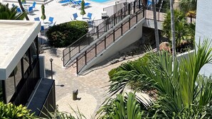 Área de piscina com cadeiras de descanso azuis e palmeiras, com vista para um corpo de água.