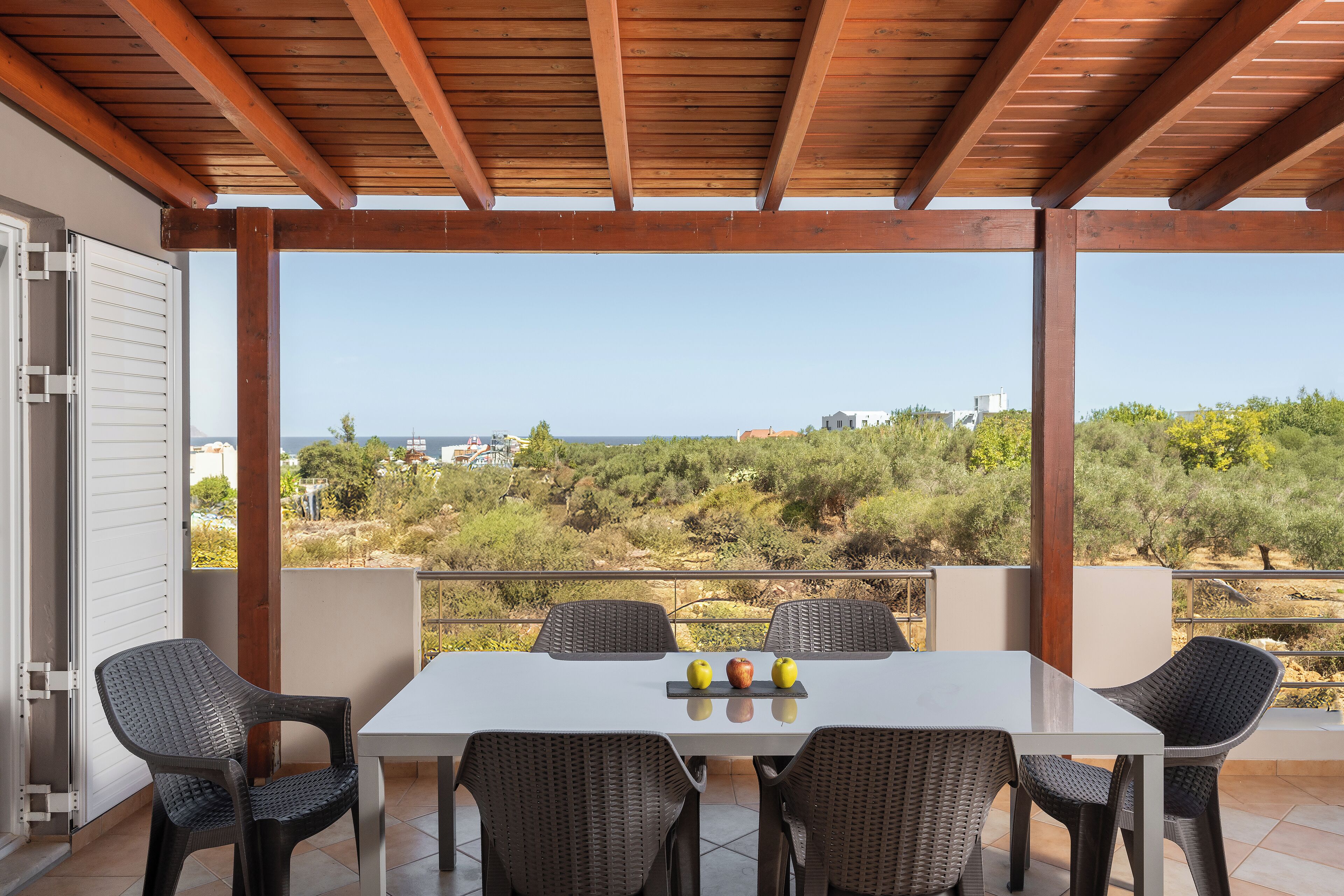 Une terrasse extérieure dotée d’un plafond en bois, d’une table blanche et de chaises en osier.