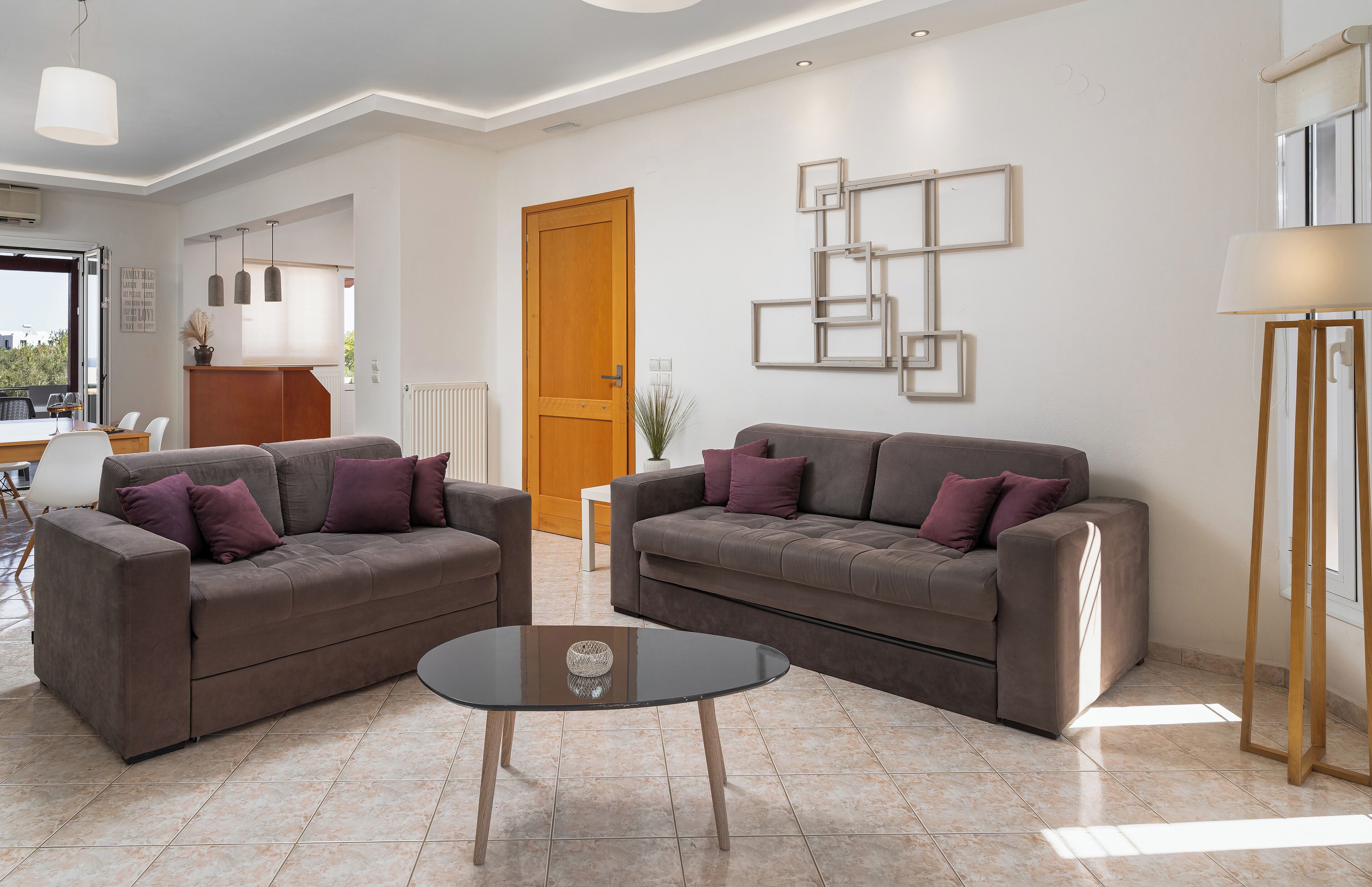 A modern living room with two sofas, a glass coffee table, and a minimalist wall art piece.