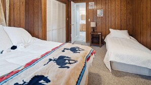 A bedroom with two beds, wooden walls, a ceiling light, and a door leading to another room.