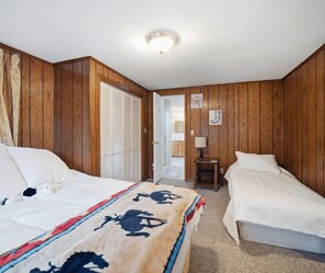 A bedroom with two beds, wooden walls, a ceiling light, and a door leading to another room.