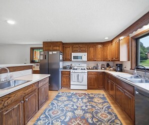 A kitchen with wooden cabinets, stainless steel appliances, a patterned rug, and a window providing a view. - 33 W. Washington - Large Village Home with Room for the Whole Family! (Ellicottville)