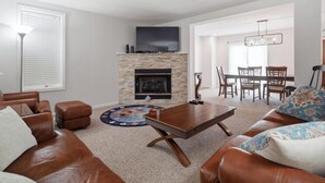 A living room with a fireplace, leather sofas, a coffee table, and a dining area with chairs and a table.