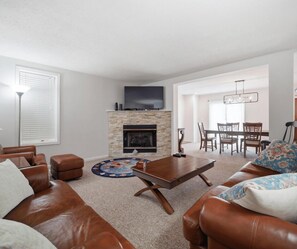 A living room with a fireplace, leather sofas, a coffee table, and a dining area with chairs and a table.