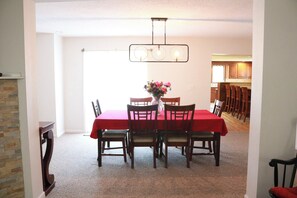 A dining room with a red tablecloth, six chairs, a vase with flowers, and a hanging light fixture.