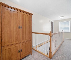 A room with a wooden wardrobe, a white railing, and a carpeted floor.