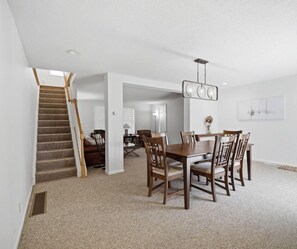 A spacious dining area with a wooden table and chairs, a staircase, and a modern chandelier. - 33 W. Washington - Large Village Home with Room for the Whole Family! (Ellicottville)