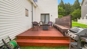 A covered patio with outdoor furniture, a barbecue grill, and steps leading to a house.