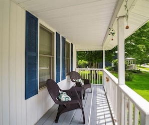 A porch with two chairs and a table, white railings, and a view of a green lawn and a house in the background. - 33 W. Washington - Large Village Home with Room for the Whole Family! (Ellicottville)