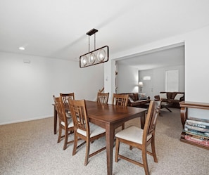 A dining area with a wooden table and chairs, a hanging light fixture, and a bookshelf with books. - 33 W. Washington - Large Village Home with Room for the Whole Family! (Ellicottville)