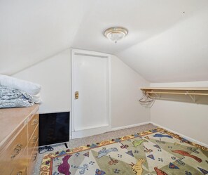 A bedroom with a sloped ceiling, a door, a small TV, a patterned rug, and a wooden dresser.