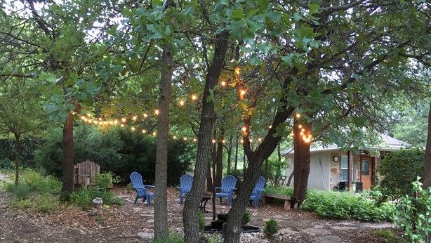 Un jardin avec des guirlandes lumineuses, un chemin de pierres et des chaises bleues.