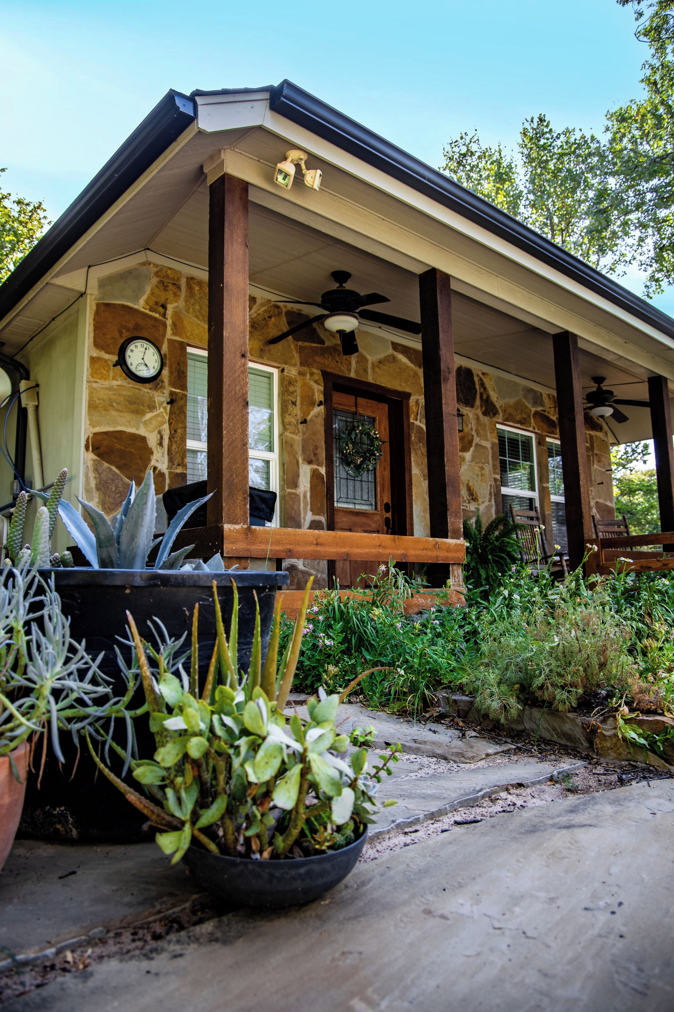 A stone house with a covered porch, a clock, and potted plants.