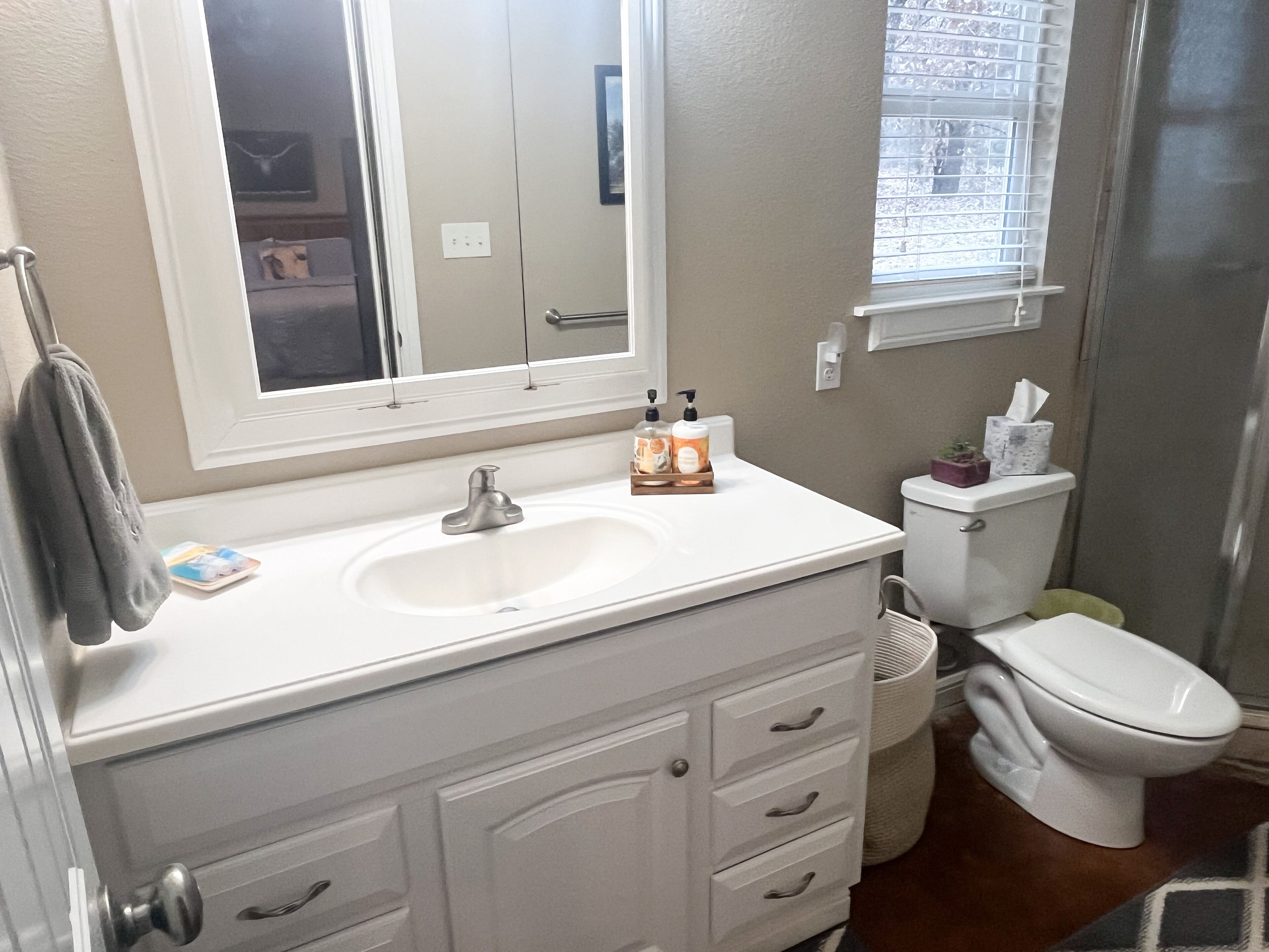 Une salle de bain avec un lavabo blanc, un miroir, des toilettes et une fenêtre.