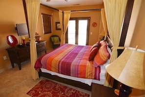 Une chambre à coucher avec un lit, des rideaux, une télévision, une chaise et une lampe.