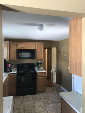Kitchen area with stove, microwave, coffee maker, refrigerator, and trash bin.