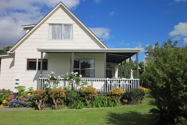 A two-story house with a gabled roof, a covered porch, and a small garden with various plants and flowers.