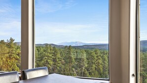 Ein Zimmer mit einem großen Fenster und Blick auf einen Wald und ferne Berge.