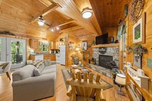 A log cabin interior with a dining area, sofa, fireplace, kitchen, and a guest sign. - Follow Me to Tennessee! Book now! Plan your Summer getaway! Choice dates remain! (Gatlinburg)