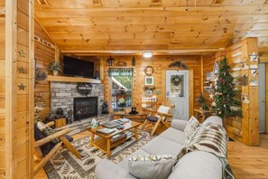 A cozy log cabin interior with a fireplace, wooden furniture, and a Christmas tree. - Follow Me to Tennessee! Book now! Plan your Summer getaway! Choice dates remain! (Gatlinburg)