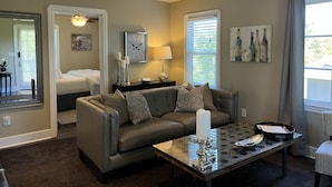 A living room with a sofa, a coffee table, a wall clock, and a window with blinds.