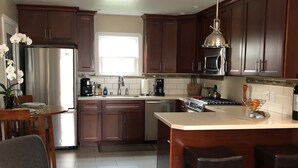 A modern kitchen with dark wooden cabinets, stainless steel appliances, a large island with bar stools, and a dining area with a chair and orchid plant.