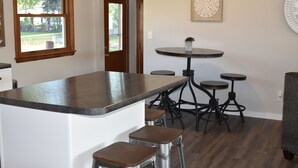 A kitchen with a central island, bar stools, and a round table with a potted plant. - Next Door To Lambeau Field /Sleeps 10+ (Green Bay)