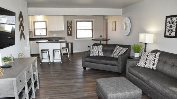 A modern living room with a grey sofa set, a coffee table, and a dining area with a kitchen counter. - Next Door To Lambeau Field /Sleeps 10+ (Green Bay)