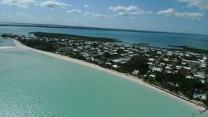 Vue aérienne d’une zone résidentielle côtière avec une plage, des maisons et une eau d’un bleu limpide.