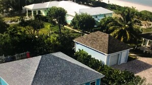 Une propriété située sur la côte, comprenant une grande maison, un bâtiment plus petit et une piscine, le tout entouré d’une végétation luxuriante et de palmiers.