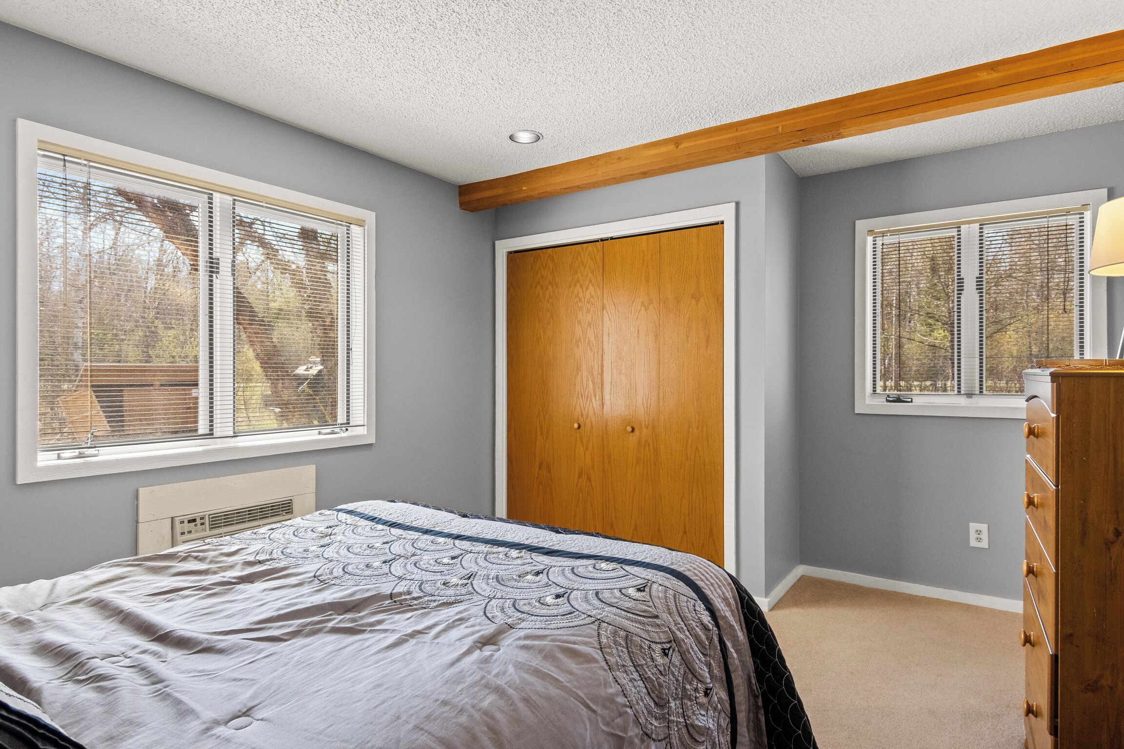 A bedroom with a bed, a wooden wardrobe, and a window with blinds.