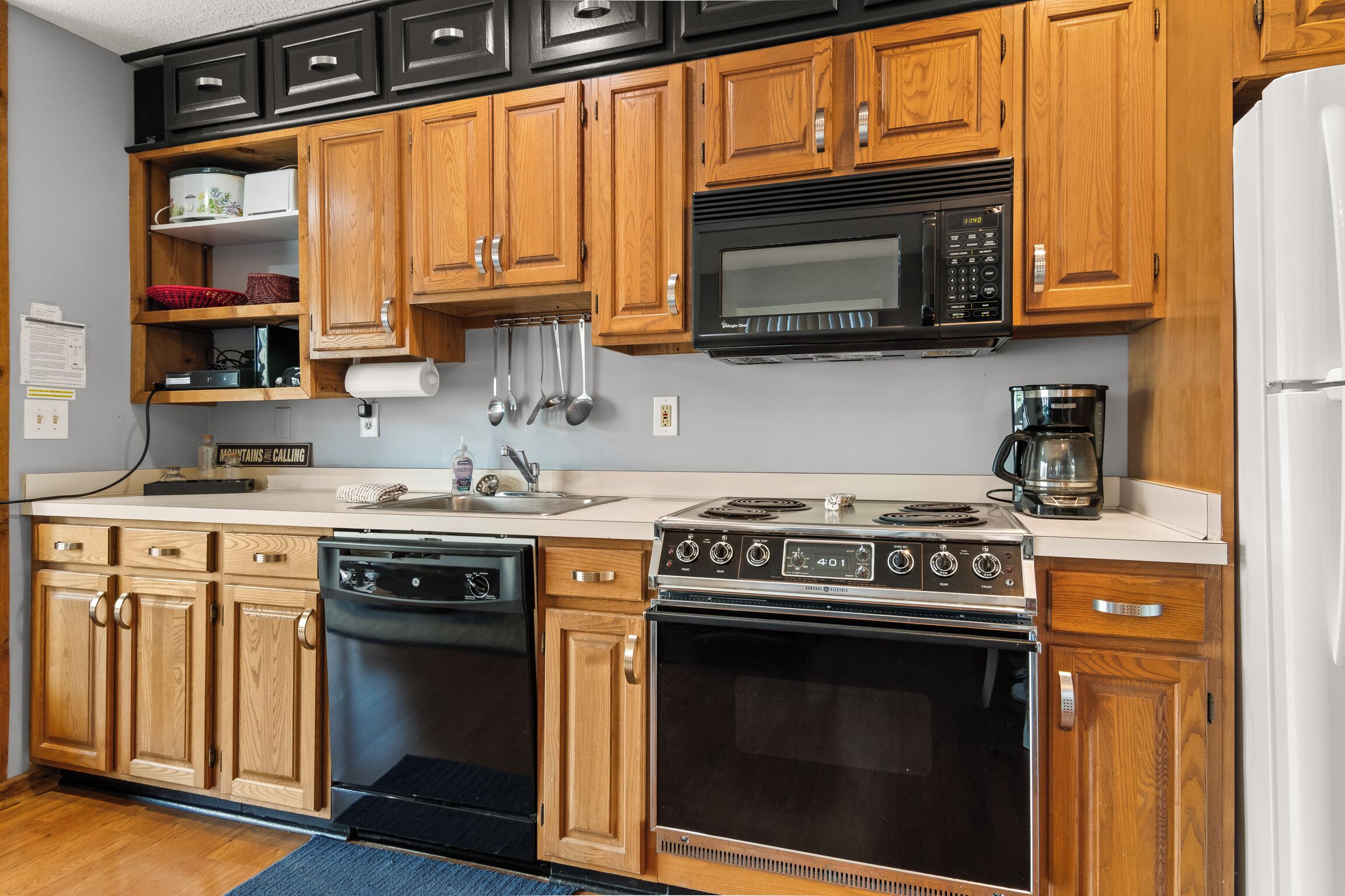 A kitchen with wooden cabinets, a black microwave, a stove, and a dishwasher.