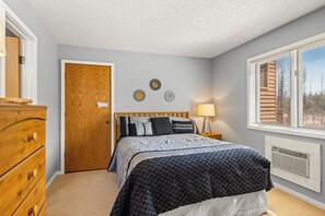 A bedroom with a bed, wooden dresser, wall decor, and a window with blinds. - 'Escape Plan' great location for year round fun (Mancelona)