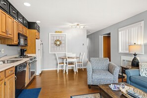 A modern kitchen with wooden cabinets, a microwave, and a dining area with a white table and chairs. - 'Escape Plan' great location for year round fun (Mancelona)