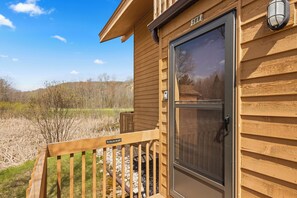 A wooden cabin with a sliding door, a 'NO GRILLING ON DECK' sign, and a view of a grassy field. - 'Escape Plan'  great location for year round fun (Mancelona)