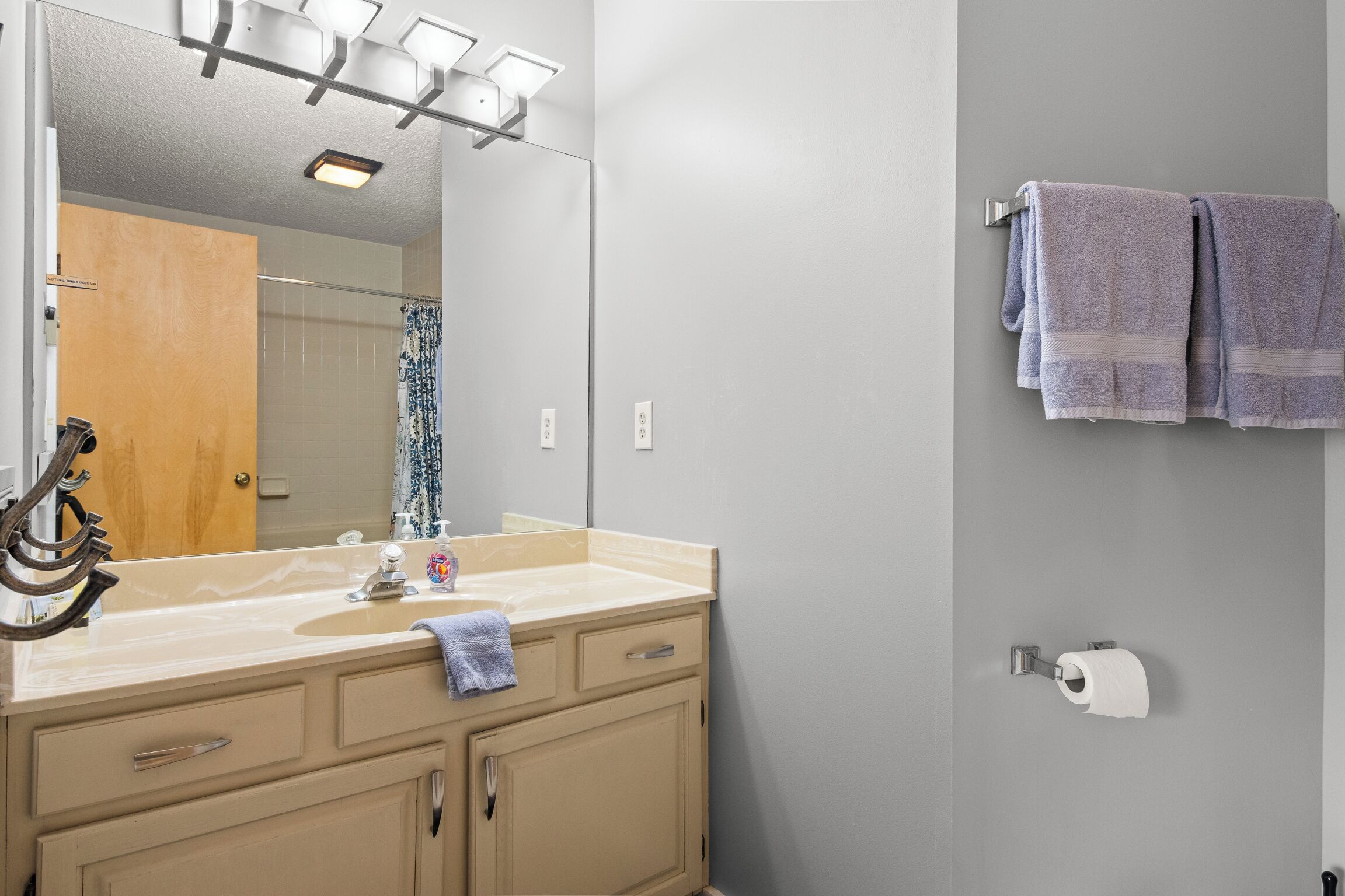 A bathroom with a sink, mirror, towel rack, and toilet paper.