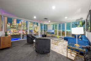 Relax in a spacious living area with a sofa, armchair, and flat-screen TV, taking in the breathtaking city view.